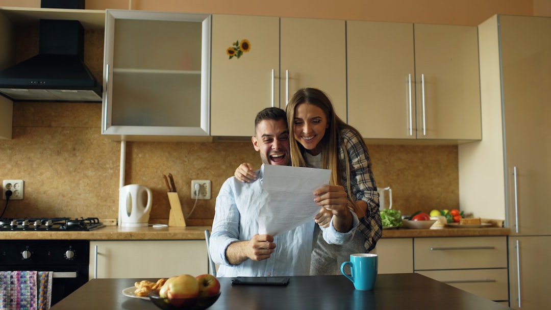 Photo by Vitaly Gariev Couple excitedly looking at a document in kitchen