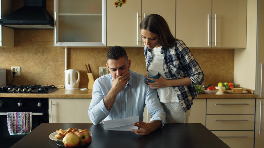 Photo by Vitaly Gariev Couple looking stressed over bills at kitchen table.